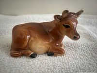 Side view of glazed brown and tan cow figurine in recumbent pose