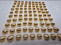 Full lot showing 100 gold-plated Om signet rings arranged in rows