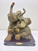 Front view of elephant family sculpture showing mother and calf with raised trunks on wooden base