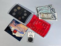 Group shot: coin set in holder, booklet, spec card, three banknotes and souvenir dollar