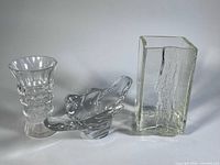 Three clear crystal/glass items: rectangular bark-texture vase, freeform bowl, faceted vase