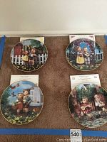 Four Hummel collector plates laid on carpet floor, each approximately 8 inches in diameter with decorative artwork and gold trims.
