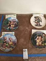 Four 8-inch Hummel collector plates displayed on carpet, showing colorful artwork depicting children in various scenes.