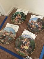 Four 8-inch Hummel plates on floor with their Certificates of Authenticity placed behind each plate, showing titles and artwork.