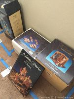 Four boxed Fontanini village pieces and Nativity Stories book on carpeted floor, showing packaging and boxed presentation.