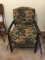 Front view of vintage wooden armchair with scenic fabric upholstery showing man fishing in creek.