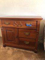 Front view of wooden vintage nightstand with carved ribbon detail and brass handles.