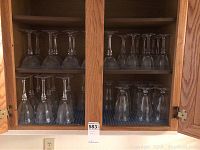 Kitchen cabinet open showing multiple shelves with crystal glasses, mostly wine glasses and champagne flutes arranged upside down.