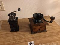 Two vintage manual coffee grinders on a wooden surface, showing general size and build.
