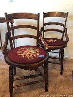Two vintage wooden chairs with carved backrests and burgundy upholstered seats with floral embroidery.
