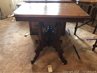Front view of vintage wooden table showing carved pedestal base and legs with wheels.
