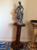 Photo of the full statue standing on the wood pedestal, showing the statue's full profile and pedestal shape.