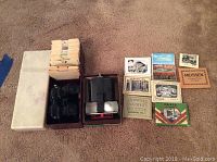 View of the white plastic box with 24 vintage View-Master reel slides and a collection of small vintage printed photo cards with historic scenes, alongside the black View-Master stereoscope.