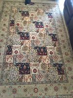 Full view of the floral design mosaic tapestry rug laid out on floor, showing the overall pattern and condition including some dirt.