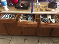 Full view of three pull-out kitchen drawers containing assorted utensils, spatulas, and flatware.