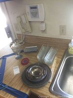 Lot contents displayed on wooden table near kitchen area including bowls, trays, plates, coasters, jar.
