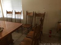 Six wooden spindle back dining chairs arranged near a dining table in a tiled room, showing the front and side views of the chairs.