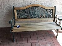 Full front view of the outdoor bench showing wood seat, metal armrests, and decorative floral patterned metal backrest with wooden frame.