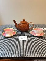 Teapot centered with two teacup and saucer sets on woven mat