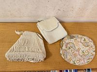 Three beaded purses: triangular white drawstring, ivory shoulder purse, round pastel clutch