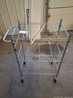 Full view of metal wire cart showing handle, three shelves, caster wheels
