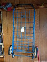 Full view of blue folding cart hanging on wall, showing wheels and handle