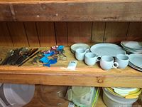 Overview of dishware, mugs, cookie cutters and flatware on shelf