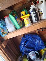 Shelf with assorted chemical jugs, potting mix bag, sprayer, tarp, planter