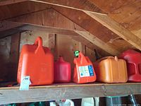 Four plastic gas cans on shelf in shed interior
