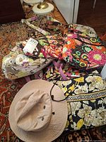Pile showing three quilted floral handbags and beige sun hat