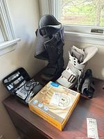 Overview of all items on tabletop: two walking boots, open case with blood pressure monitor, wrist brace, boxed pill dispenser