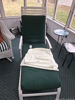 Full view of lounge chair with green cushion and additional white towel on seat