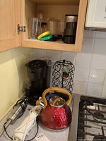 Overview of countertop showing coffee brewer, pod rack, kettle, immersion blender, electric knife and Magic Bullet cups in cabinet