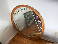 Full view of round mirror leaning against wall showing wood frame and painted motifs