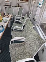 Group of six white aluminum patio chairs with green leaf sling fabric