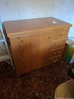 Full view of closed oak-finish sewing cabinet showing drawers and door