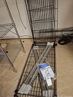 Unassembled black wire shelves and grey posts on floor