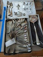 Overview of all silverplate pieces on trays showing ladle, tongs, spoons and picks