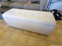 Beige upholstered storage bench with tufted lid and nailhead trim