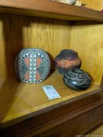 Three pottery pieces on shelf: blackware bowl, geometric seed pot, raku jar