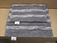 Stacked gray striped bath rugs showing size difference and attached brand tags