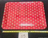 Top view of red crest-patterned tray with tape measure showing length