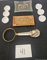 front view of all items: glass logo ashtray, six white ashtrays, train relief ashtray, magnifying glass