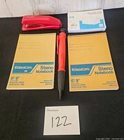 All five items laid out: two notebooks, stapler, index card pack, red hand tool