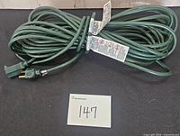 Coiled green outdoor extension cord with safety labels and three-prong plug visible, lot number card present