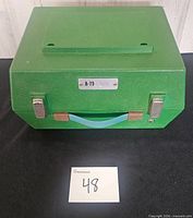 Closed green suitcase-style A-79 talking book machine showing handle, latches and model plate