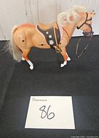 Left side view of plastic toy horse displaying saddle and bridle