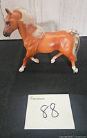 Right side view of tan plastic horse with white mane and braided tail