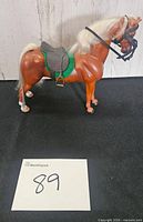 Left side view of plastic horse with saddle, bridle and green pad