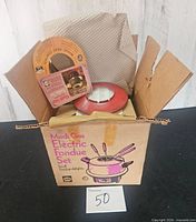 Open box showing fondue lid and printed Mardi-Gras Electric Fondue Set graphics